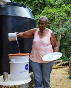 Woman pouring water into a water filter, standing in front of a rainwater tank